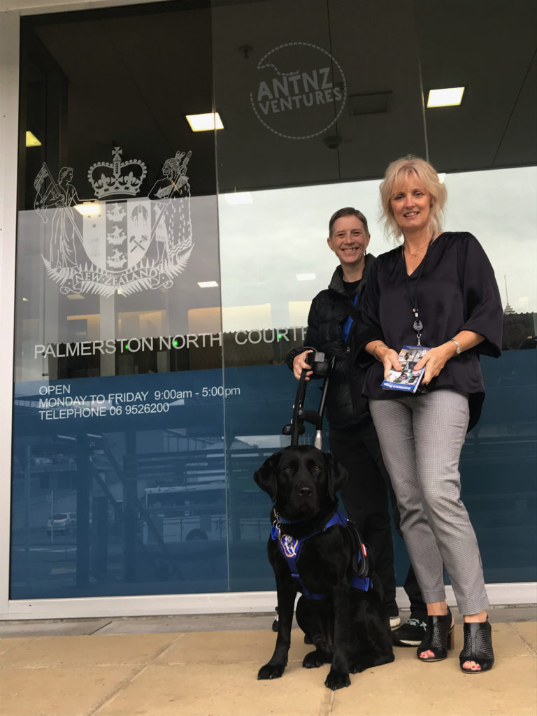 A photo of Antnz (Antnz) and Vicky (right, judges clerk) standing in front of the Palmerston North Courthouse with the NZ Coat of Arms seen.