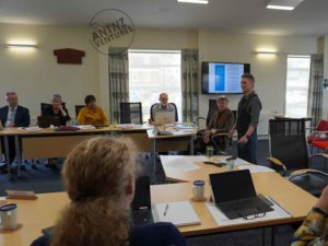 Antnz is standing in a formal board room to the right of frame. There are people sitting on tables facing Antnz to the left.