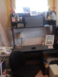 A picture of a computer desk that has been cleared and cleaned, on the top shelves are nick-nacks and pictures. On the desk is a lamp and a framed picture.