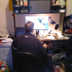 A picture of Antnz, sitting at a computer desk. A large monitor can be seen, with a laptop over Antnz shoulder on the left of picture