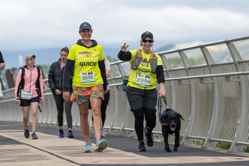 Antnz on the right with ADNZ Raven, Wendy on the left. Raven is to the right of Antnz, with her tongue slightly out and her ears flapping. Antnz is pulling a peace sign at the camera. They are walking over a bridge