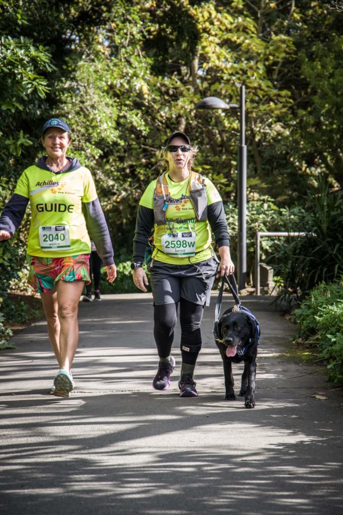 Wendy, Antnz and ADNZ Raven are walking on a pathway with a lamppost and bush in the background.