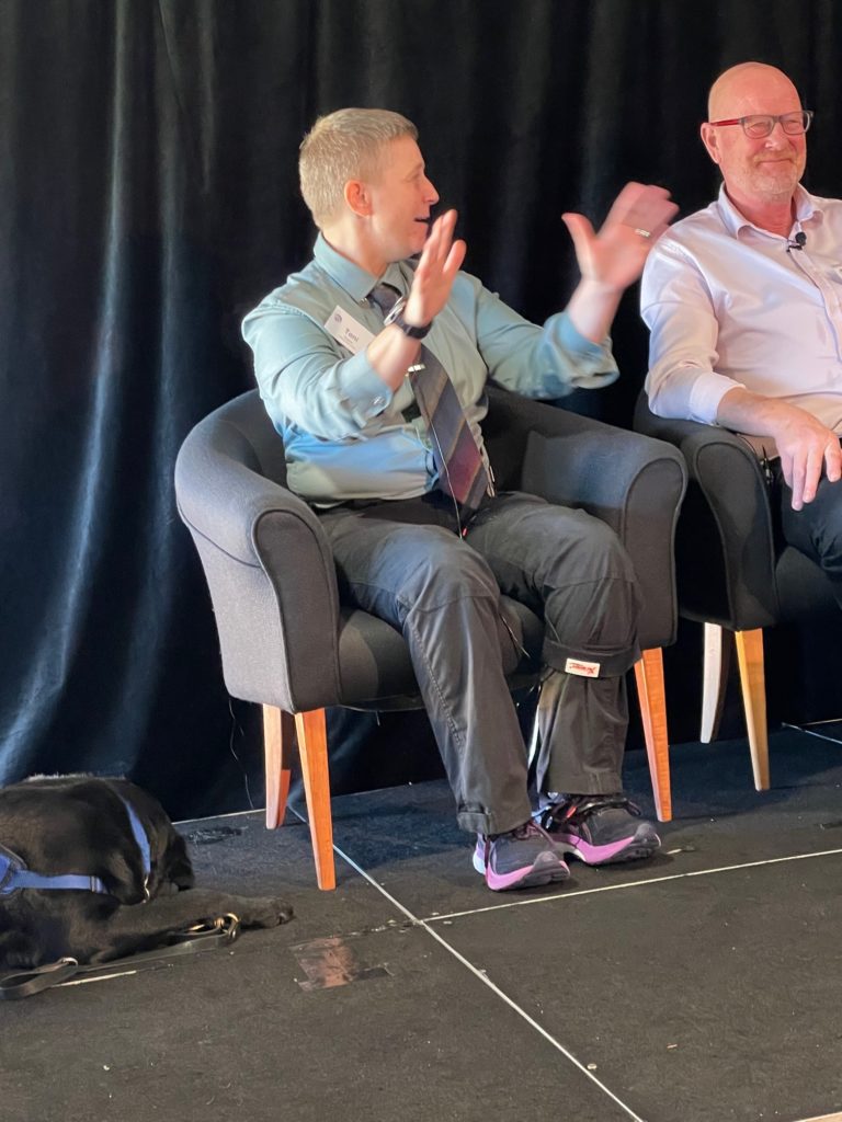 Antnz is sitting next to a man with glasses. Antnz is gesturing with her hands as she talks.