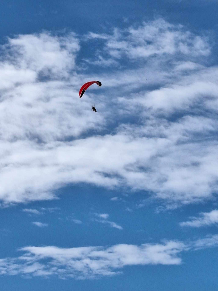 A red paraglider in a blue sky with a few puffy white clouds